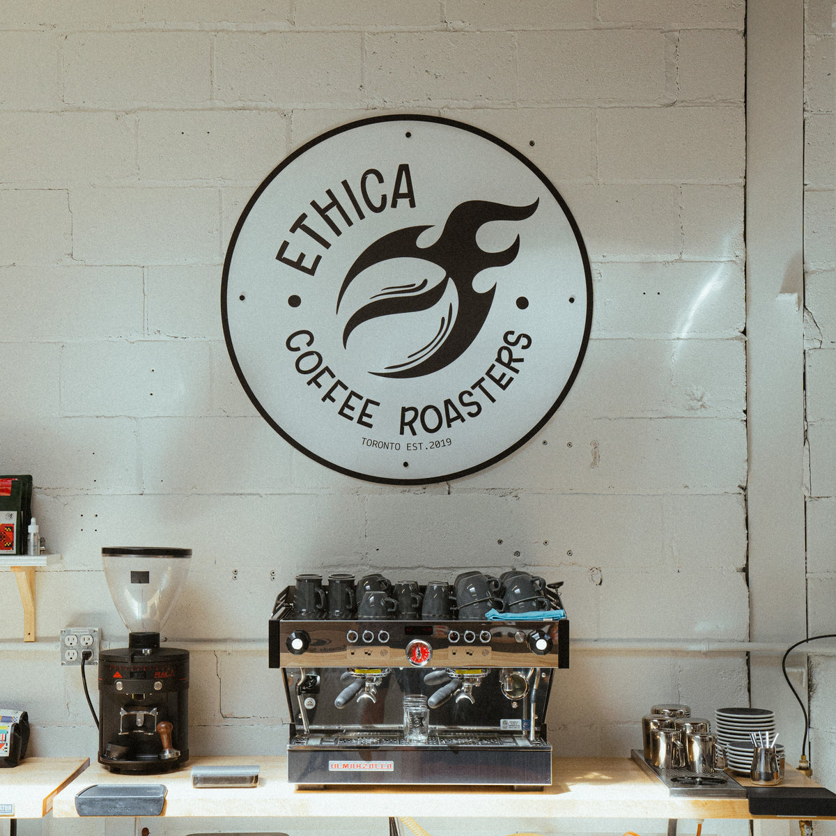 ethica roasters logo hung on the wall above an espresso machine