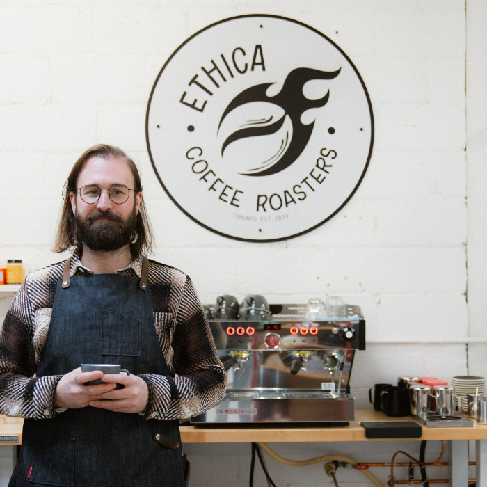 man standing with a cup of specialty coffee in front of ethica logo