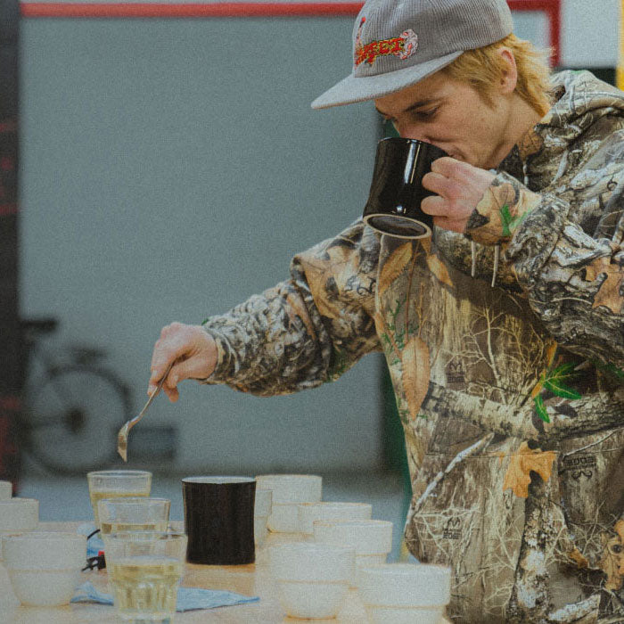 person drinking a cup of coffee while preparing more coffee